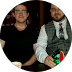 Two men sitting at a table, one wearing glasses and the other a grey vest.